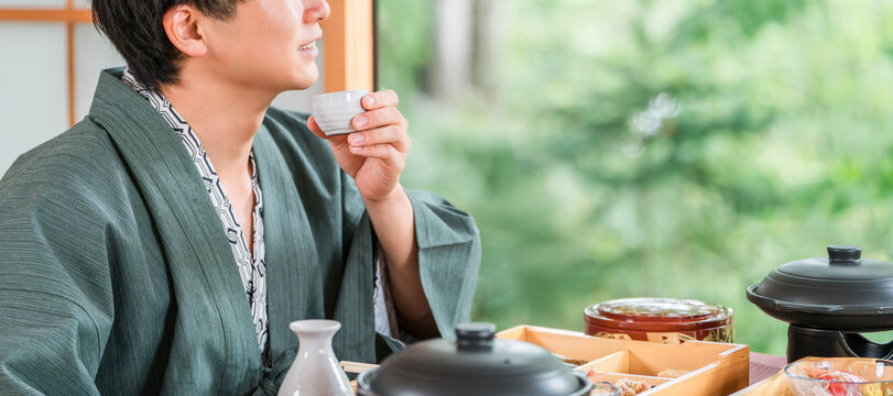 Young Asian man drinking sake with kaiseki cuisine at a ryokan (room dining, kaiseki cuisine, meal, luxury)
