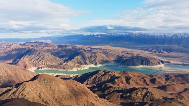 Dramatic view of snow-capped mountains reflected in a tranquil Orto Tokoy reservoir. Clear sky with scattered clouds enhances the vast, serene atmosphere.