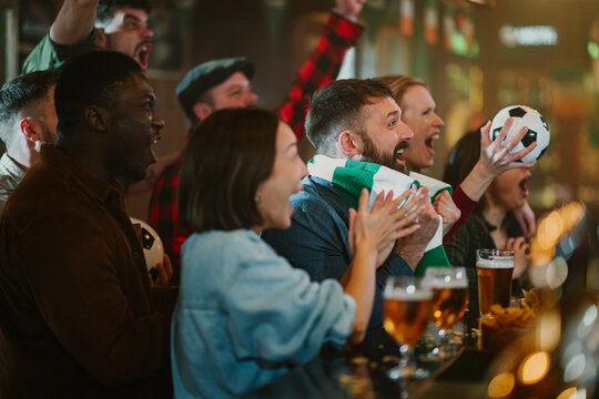 Diverse soccer fans watching game and celebrating victory in bar