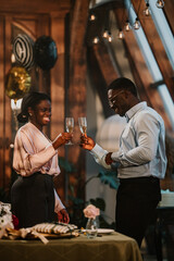 African american couple smiling, clinking champagne glasses, celebrating an occasion, enjoying a...