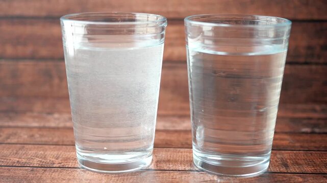 Two glasses of water on a wooden table one with bubbles and one clear