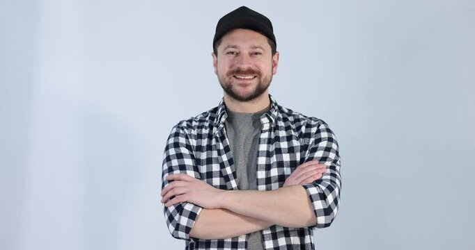 Smiling long-haul truck driver in baseball cap and checkered shirt posing with crossed arms on grey background