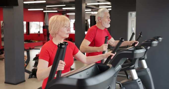 Senior couple training on elliptical machines in gym
