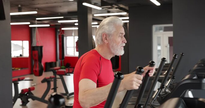 Senior man training on elliptical machine in gym