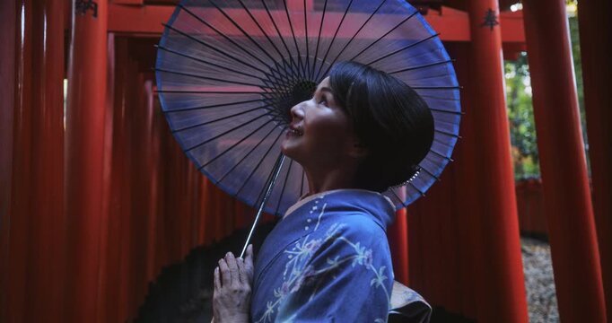 Smiling Japanese woman in kimono standing amongst many tori gates
