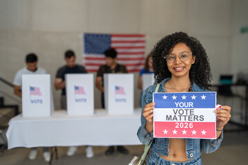 African American woman smiles holding a 'Your Vote Matters 2026' sign at a US election polling...