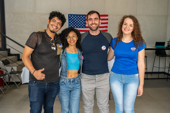 diverse group of friends smiling at a US election polling station, wearing 'Vote 2026' buttons on their clothing, American flag in the background, democratic process, right to vote in America.
