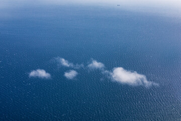 Aerial view of a serene blue ocean with scattered, wispy clouds reflecting on its surface, evoking tranquility and vastness. Perfect for themes of travel, nature, freedom, environmental concepts