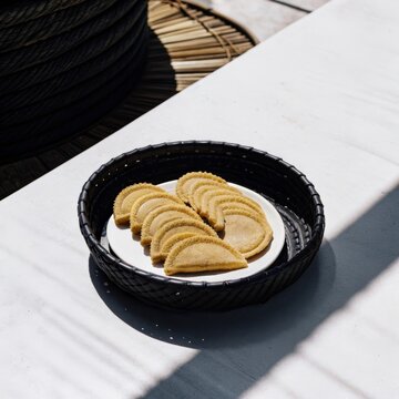 A plate of golden kuih kapit, crispy love letters cookies arranged in a black wicker bowl on a white table.