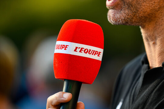 French channel "L&rsquo;&Eacute;quipe" red microphone held by an unrecognizable journalist during an outdoor interview, symbol of media coverage and live news reporting.