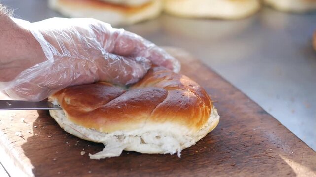 Close up of hands in gloves slicing a bread roll on a wooden board preparing food
