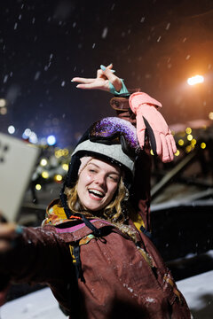 Teen enjoys the winter night by taking a selfie while wearing a ski helmet and gloves during a snowy street festival