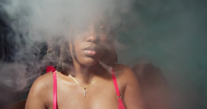 A woman with a rich, dark complexion in simple cotton lingerie, smoking