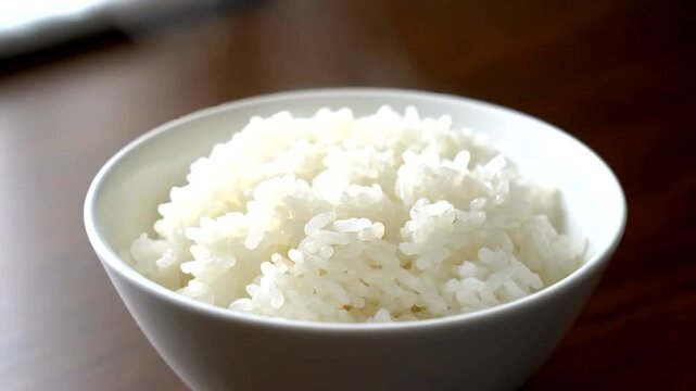 A close-up shot of a white bowl filled with freshly cooked, fluffy white rice, ready to be served as a staple meal.