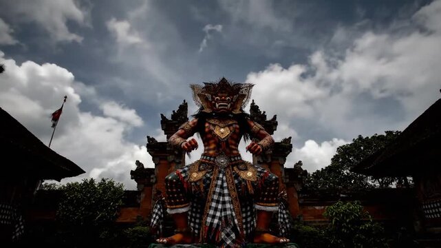 A dramatic low-angle shot of a towering, ornate traditional Balinese guardian statue under a cloudy, atmospheric sky.