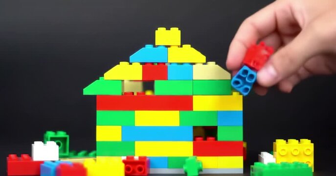 Hand adding colorful blocks to a toy house structure