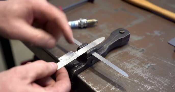 Hands adjust metal feeler gauge in tool clamp on workbench