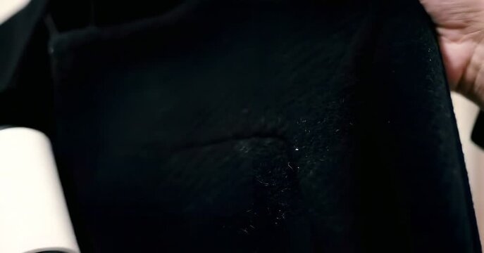 Hands using lint roller on dark fabric clothing