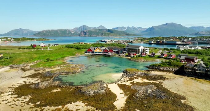 Island village and turquoise lagoon at Sommaroy in Troms, Norway, wide pullback drone shot.