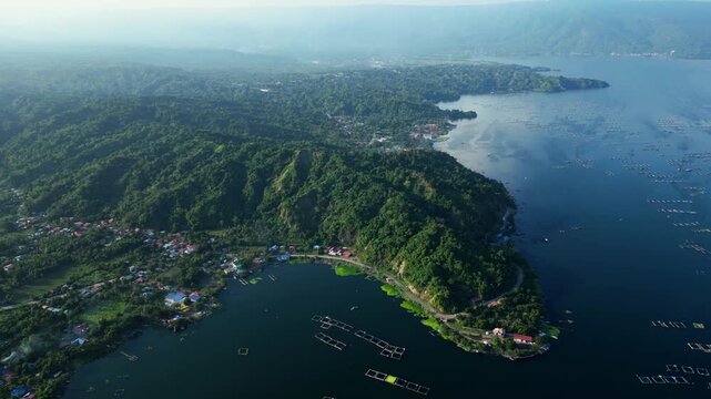 Horizontal l drone perspective of geometric ocean fishpond grids with tiny boats and rising behind mountains in Agoncillo, Batangas Philippines.