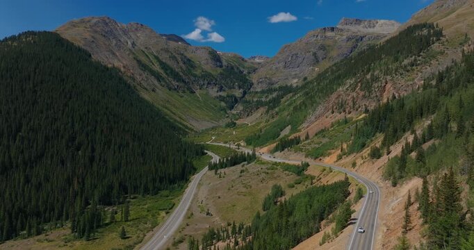 Aerial of mountain road winding by forested San Juan valley under blue skies, Million Dollay Highway Colorado USA