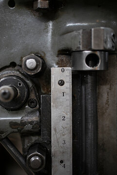 Close-up of a metal ruler measuring the precise movement of a threaded rod on industrial machinery