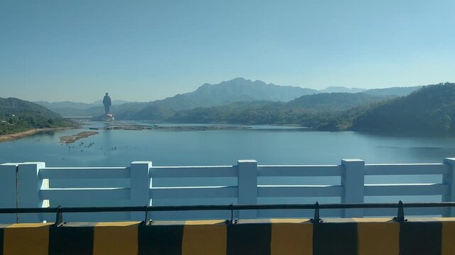 Statue of Unity in Ekta Nagar Gujarat India seen from Narmada River bridge, iconic Sardar Patel monument with mountain landscape and dam water reservoir background.