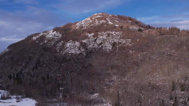 Aerial drone footage flying directly toward The Butte in Palmer, Alaska as it fills the frame. The camera then executes a smooth sweeping left turn away from the mountain, pivoting toward distant snow