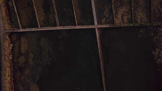 High top down aerial drone shot of the Aveiro salt pans, showing a dark brine evaporation pond framed by narrow dikes and mud banks, part of Salinas de Aveiro within the Ria de Aveiro lagoon system