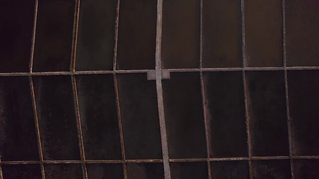 Geometric grid of dark brine evaporation ponds and narrow dikes forms the Salinas de Aveiro salt pans inside Ria de Aveiro coastal lagoon in Portugal, top down drone reveal shot.