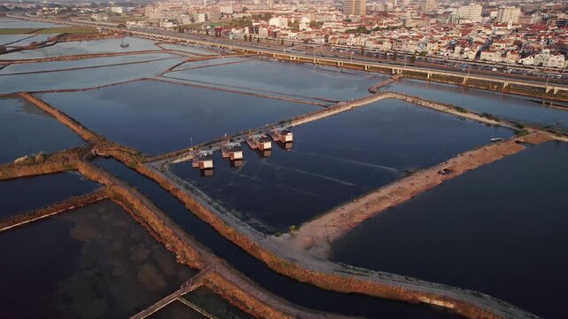 alinas de Aveiro salt pans in Portugal form a geometric grid of brine evaporation ponds divided by narrow dikes and saltwork huts, with Aveiro city visible beyond the Ria de Aveiro lagoon, drone wide