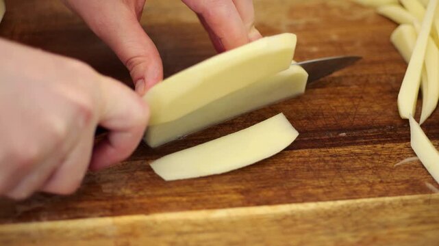 Slicing raw potatoes into french fries on cutting board