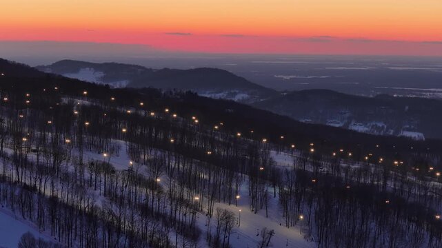 Aerial drone view of illuminated Bromont ski resort slopes at dusk, Quebec, Canada in winter. g.
