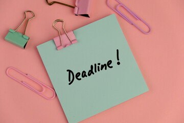 a notepad next to alarm clock with text of deadline on pink background as a memo or message concept.