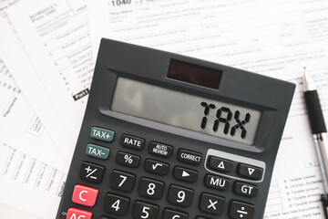 Calculator displaying the word &ldquo;TAX&rdquo; placed on official tax forms. Ideal for topics related to income tax, tax calculation or finance management.