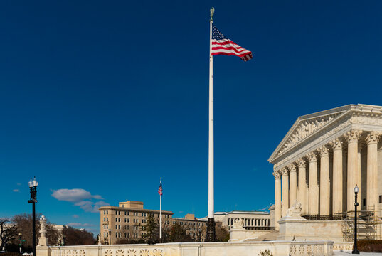 American flag flying above supreme court architecture. Judicial branch concept with historic neoclassical building. Democracy and legal system symbol in capital city.