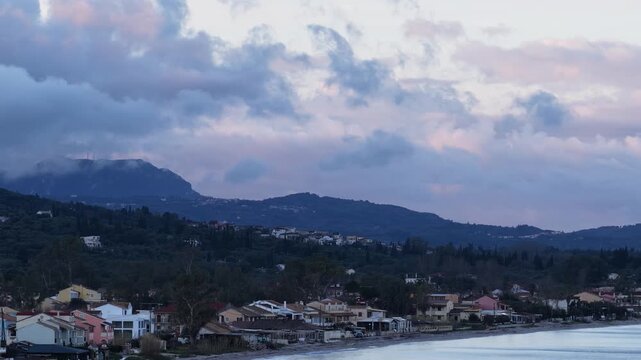 Aerial View of Acharavi Beachfront Houses at Sunrise with Dramatic Purple Clouds and Mountains, Northern Corfu Island Greece, serene coastal landscape and architecture