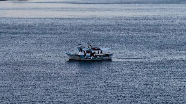 Small traditional fishing vessel navigating through the calm blue sea near Acharavi, Corfu island, Greece, clear water and ripples, authentic Greek island maritime lifestyle and transportation, scenic