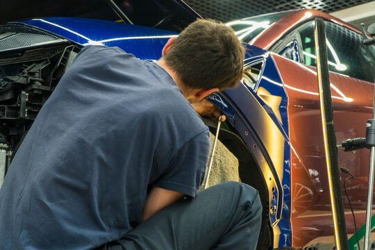 Process of paintless dent repair on car body. The mechanic at the auto shop with tools to repair dents in car body. Body repair. PDR. A specialist repairs a dent on the car body without painting.