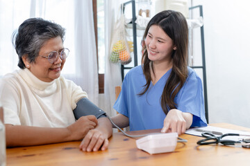 Obraz premium Nurse measuring blood pressure of senior women at home. Elderly patient receiving healthcare service, hypertension check, medical consultation and home care concept.