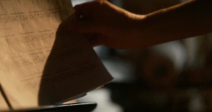 Cinematic close-up female hand gently taking and flipping sheet music pages with soft piano bokeh in the background. blurred keyboard lights create atmospheric sheet music, Moscow Russia 02.17. 2026