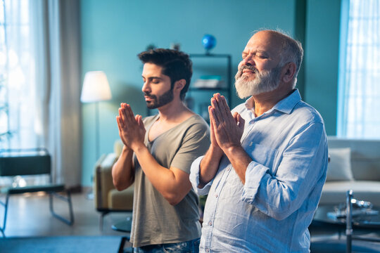 Indian senior dad and adult son performing Hindu prayer ritual indoors with folded hands
