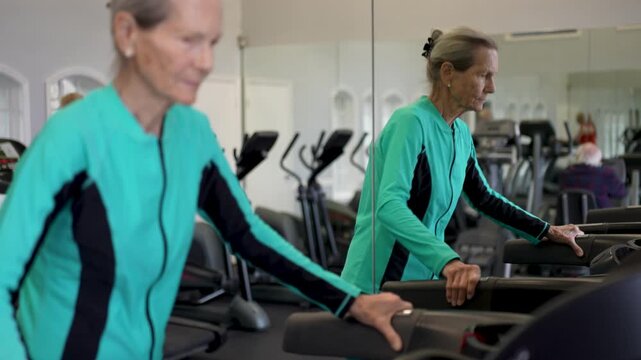 Elderly woman exercises on treadmill in gym. She focuses on her workout with determination and stays active for her health.