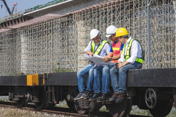 Group of engineers and site managers sitting on a train wagon discussing construction blueprints at a massive infrastructure project site, Railway construction team reviewing technical plans