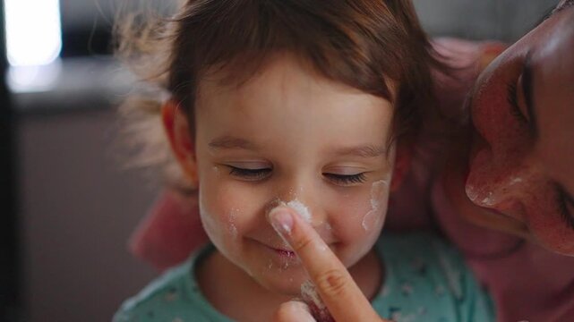 A Joyful Moment: A Young Child with Cream on Her Face, Sharing a Tender Interaction with an Adult, Captured in Two Frames of Playful Engagement and Smiles