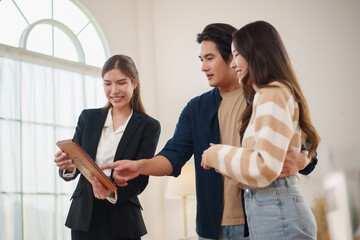 Asian female real estate agent presenting house information on tablet to couple