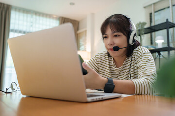 Asian female student concentrating on online class using laptop and headset