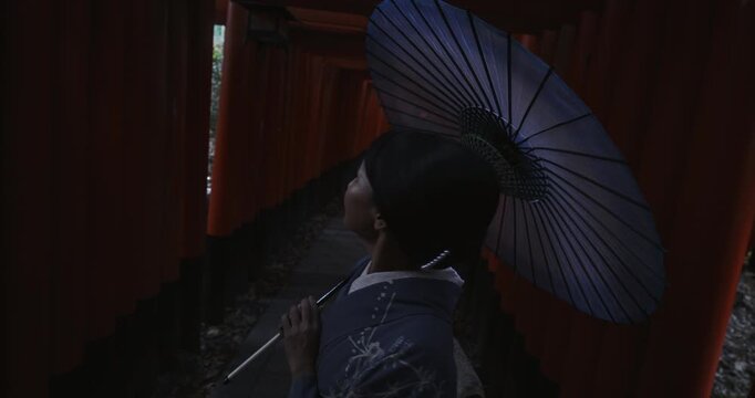 Happy Japanese woman in cultural clothes standing under torii gates as shadow approaches her