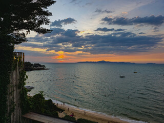 Obraz premium A breathtaking sunset over a tropical bay with people relaxing on the beach and boats anchored in the calm sea under a dramatic cloudy sky