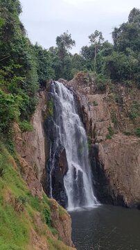Tall waterfall flowing down rocky cliff surrounded by green forest